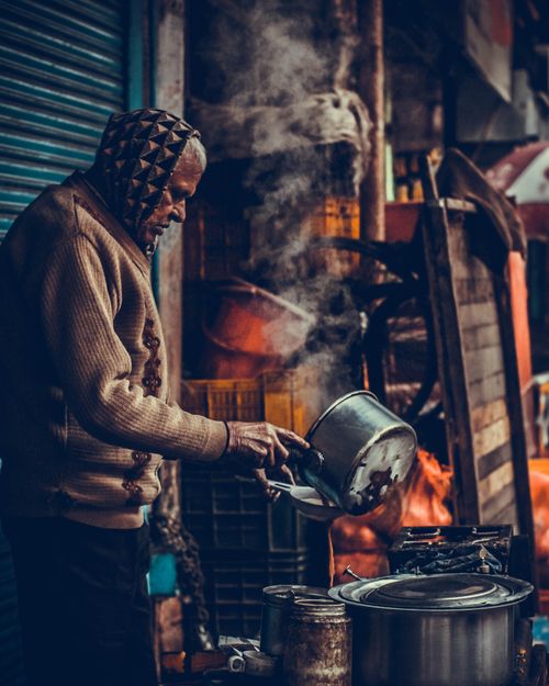 Free Senior man prepares food outdoors, steam rising from pot in bustling Srinagar street. Stock Photo