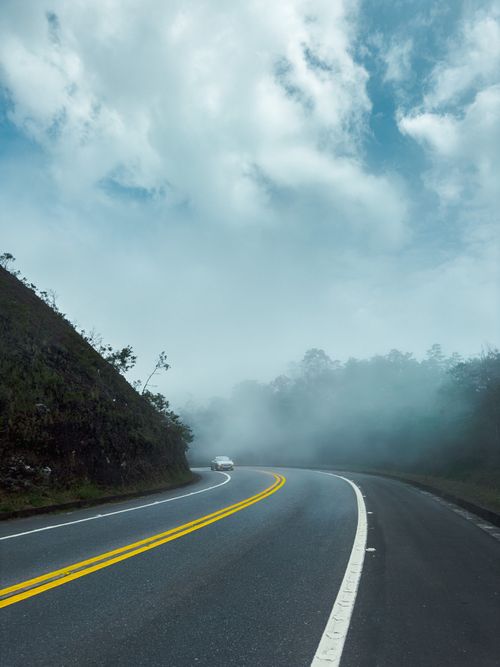 Free A winding highway in Brazil enveloped by fog and lush greenery, creating a serene travel scene. Stock Photo