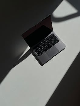 Artistic overhead view of an open laptop casting shadows on a flat surface.