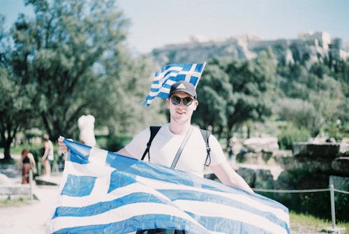 Young Man in Sunglasses Holding a Greek Flag 