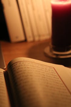 An open book with Arabic script by candlelight, creating a warm, cozy atmosphere.