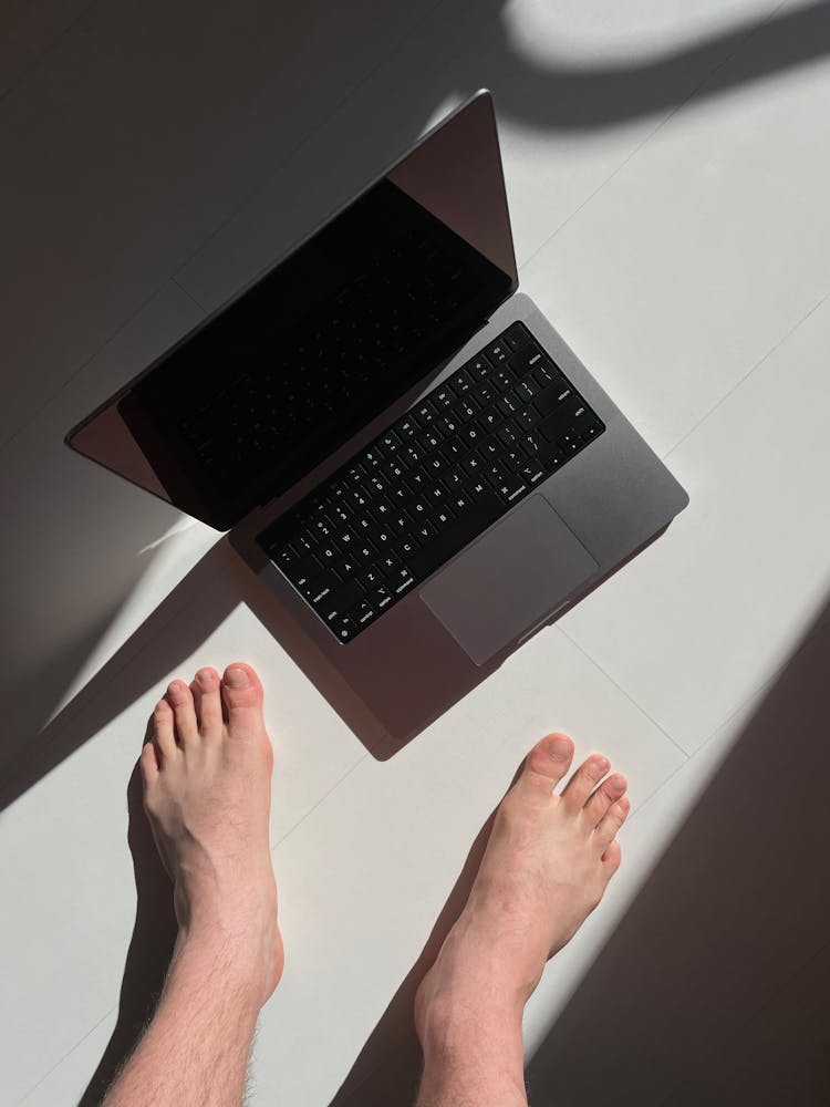 A Man Standing Barefoot Next To A Laptop 