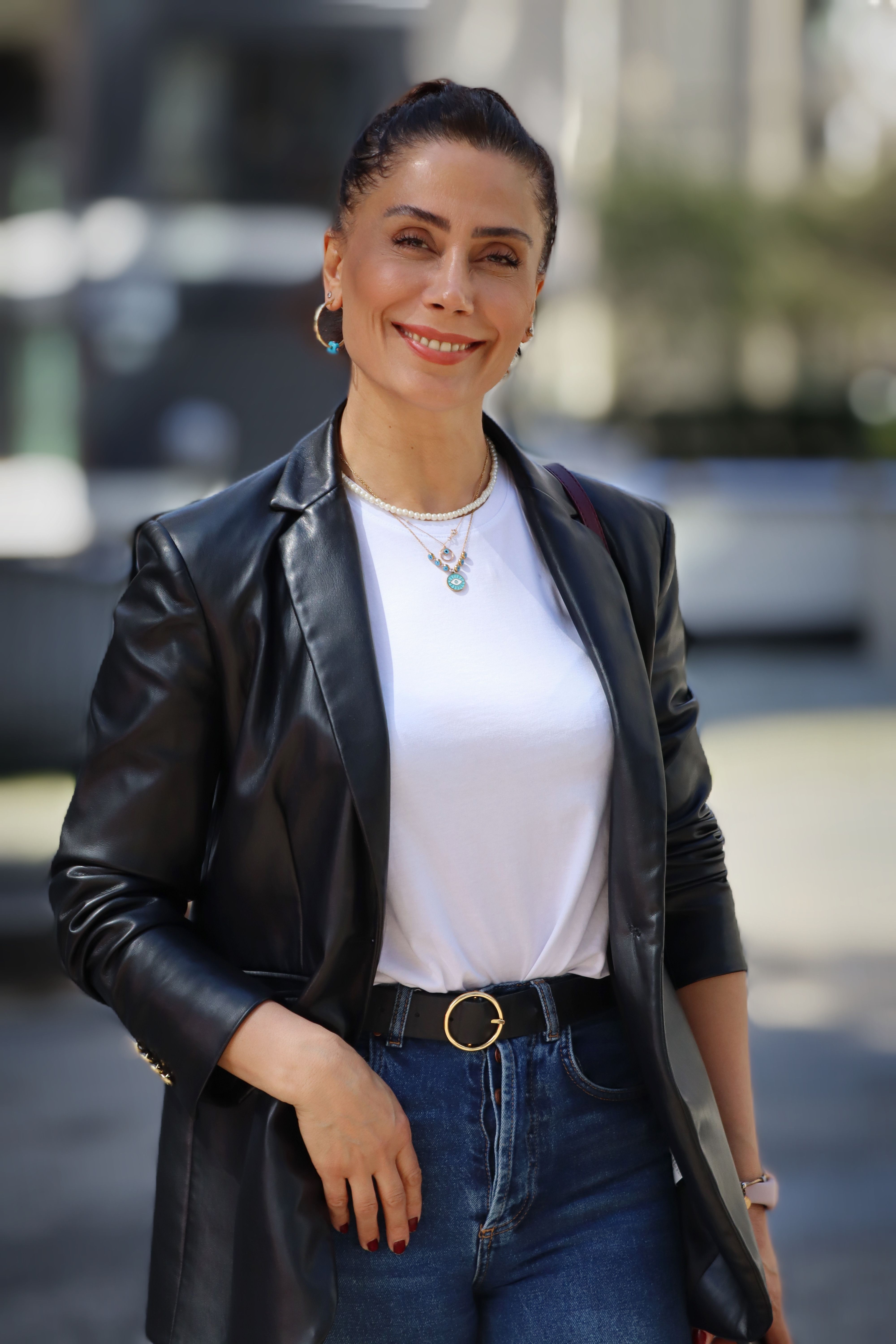 A fashionable woman poses outdoors in a leather jacket and jeans, embodying modern urban style.