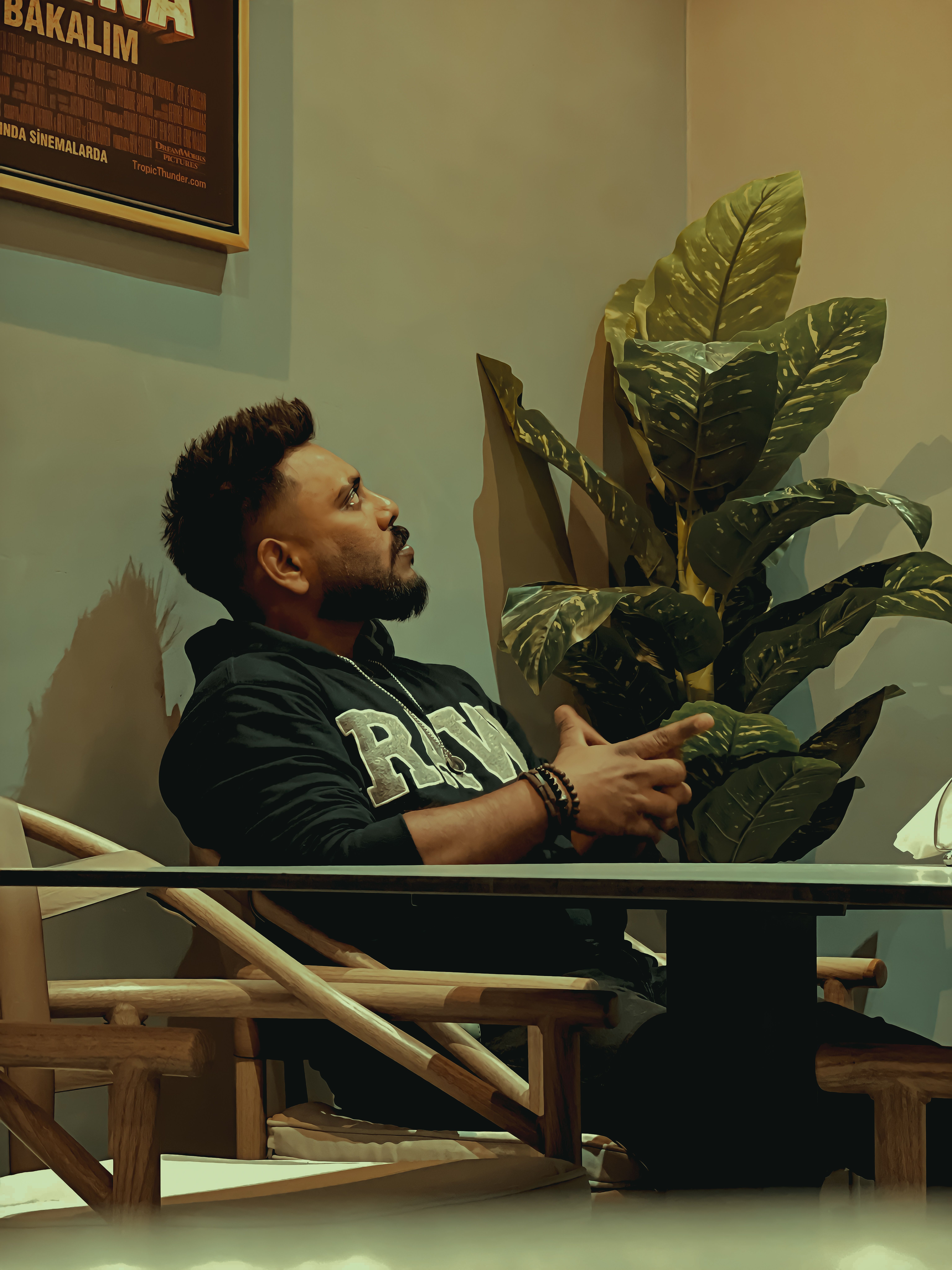 Man sitting indoors, gazing thoughtfully. Cozy atmosphere with potted plant.
