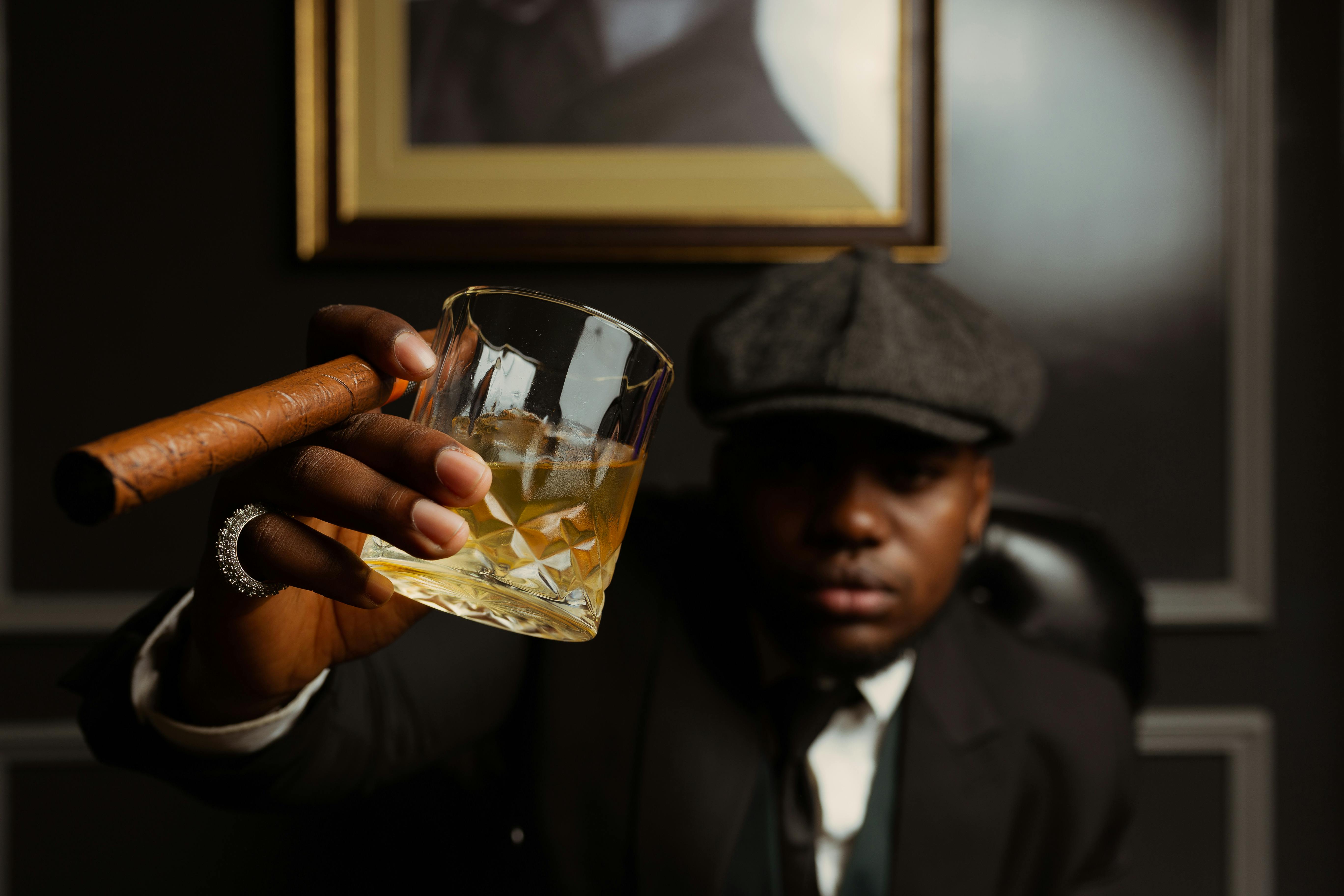 man in a peaked cap drinking whisky and smoking a cigar