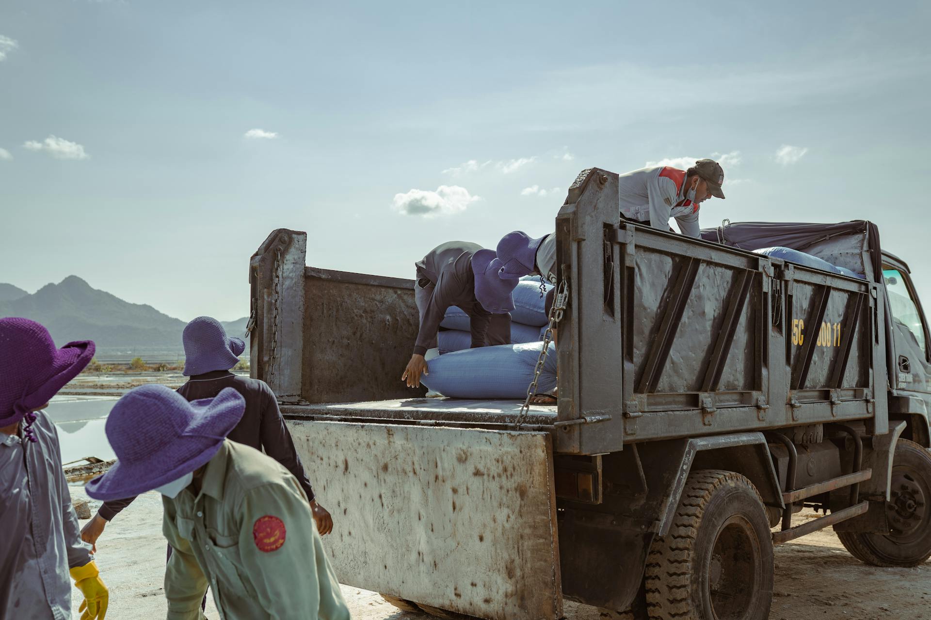 Team of workers unloading barrels from a truck on a clear day with mountains in the background.