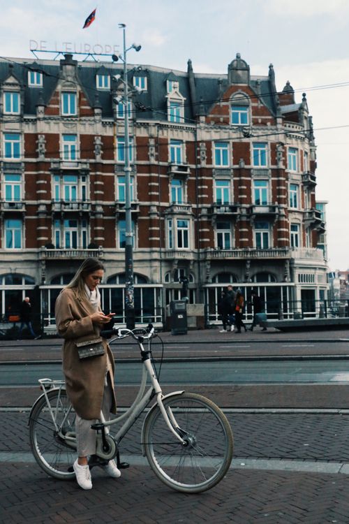 Free A woman stands with her bicycle on a European city street in front of a historic building. Stock Photo