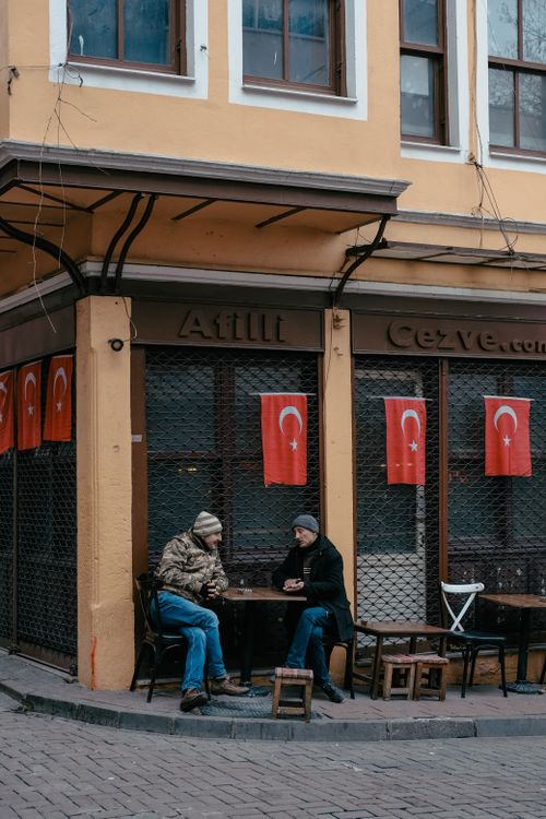 Free Two men sitting at a street cafe in İstanbul under Turkish flags. Stock Photo