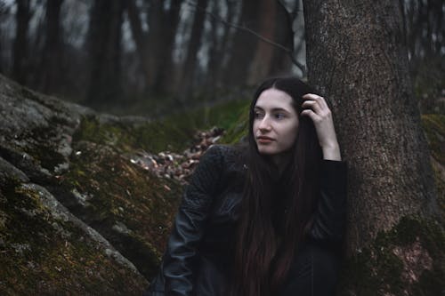 Young Woman Sitting by a Tree in a Forest and Looking Away 