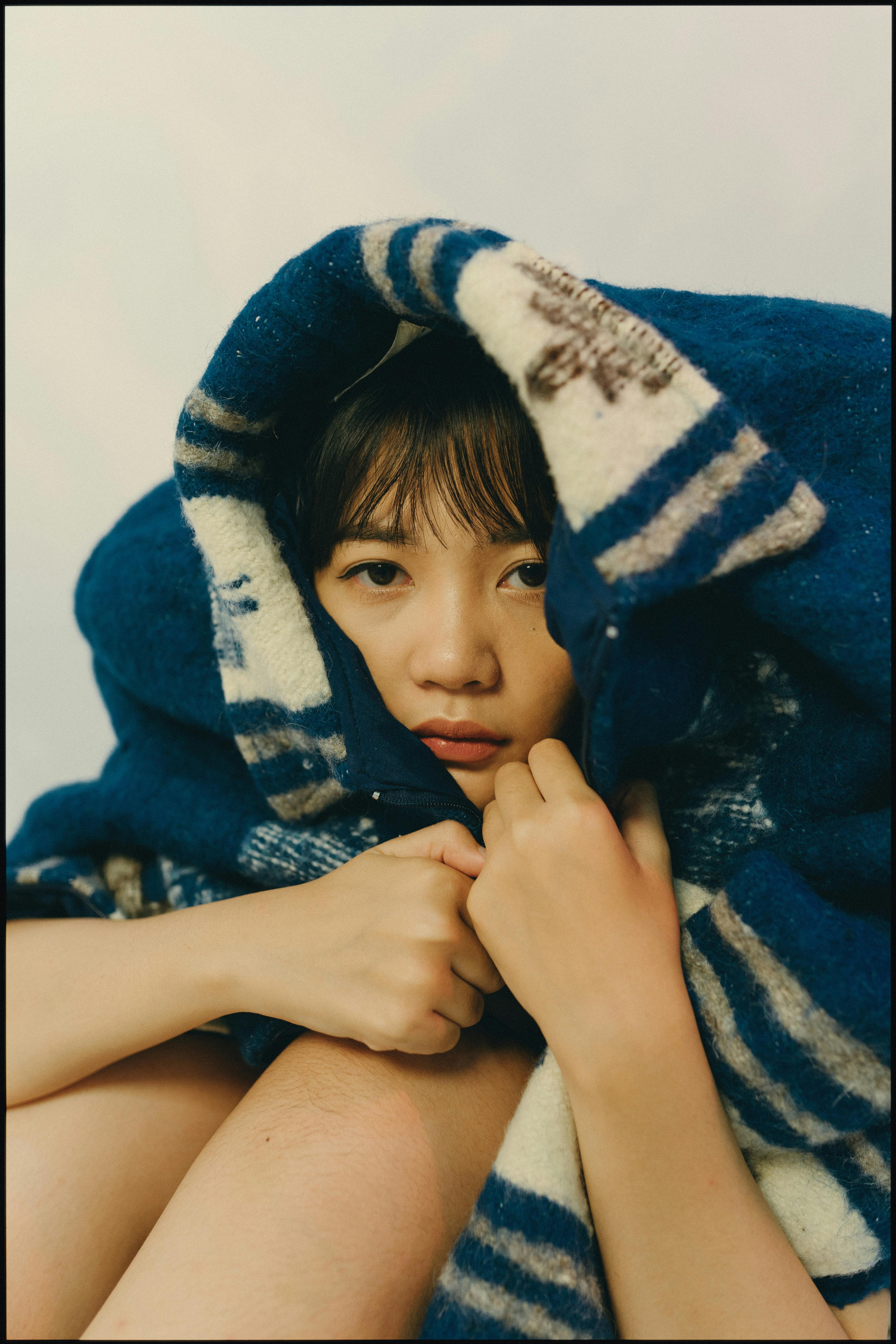 Intimate portrait of a woman wrapped in a blue-striped blanket, conveying warmth and comfort.