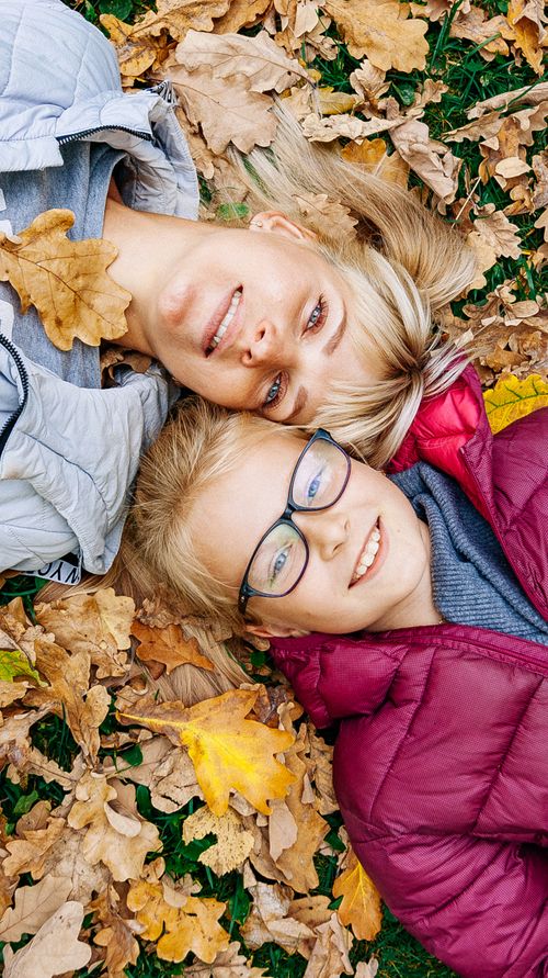 Free Mother and son enjoying a joyful moment lying in fall leaves, smiling at the camera. Stock Photo