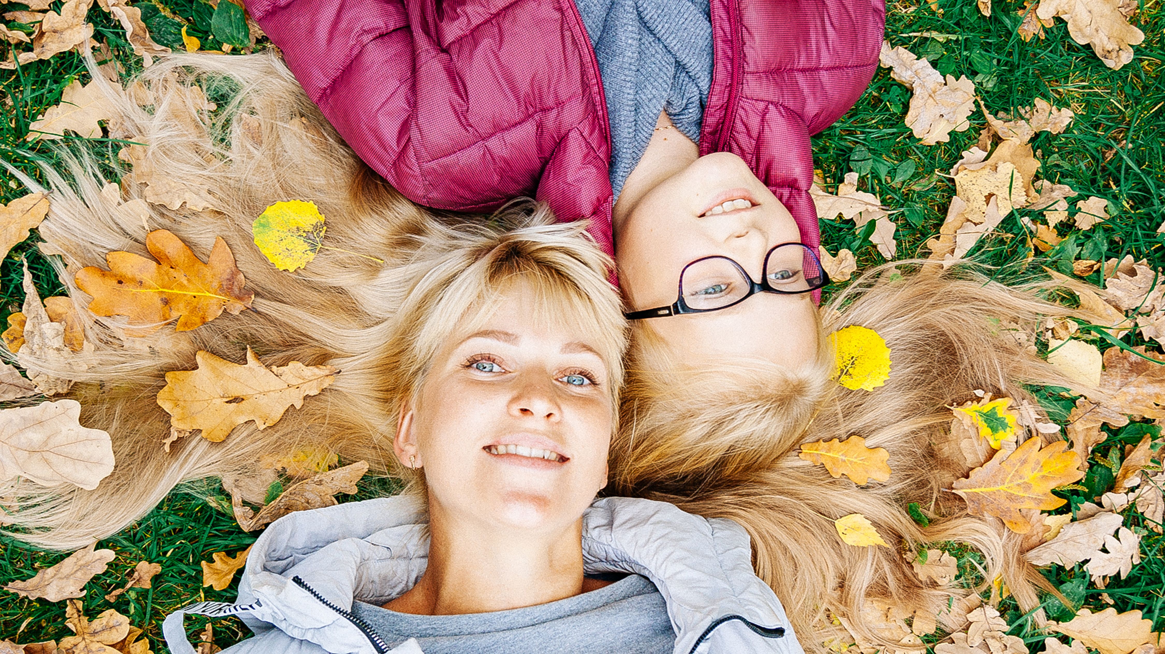A joyful mother and daughter lie on fall leaves, smiling brightly.
