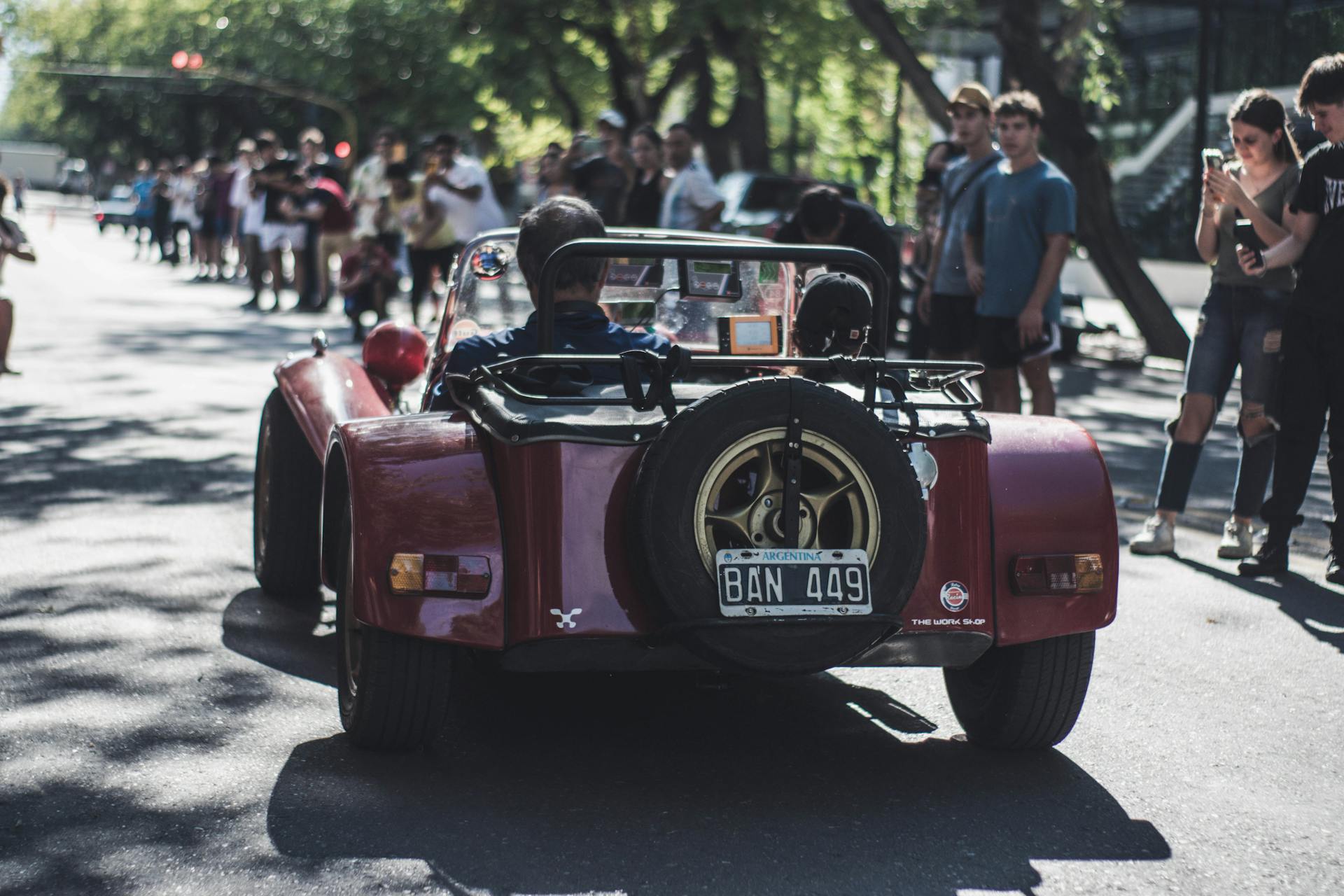 A vintage convertible car participating in an urban street rally with spectators lining the road.