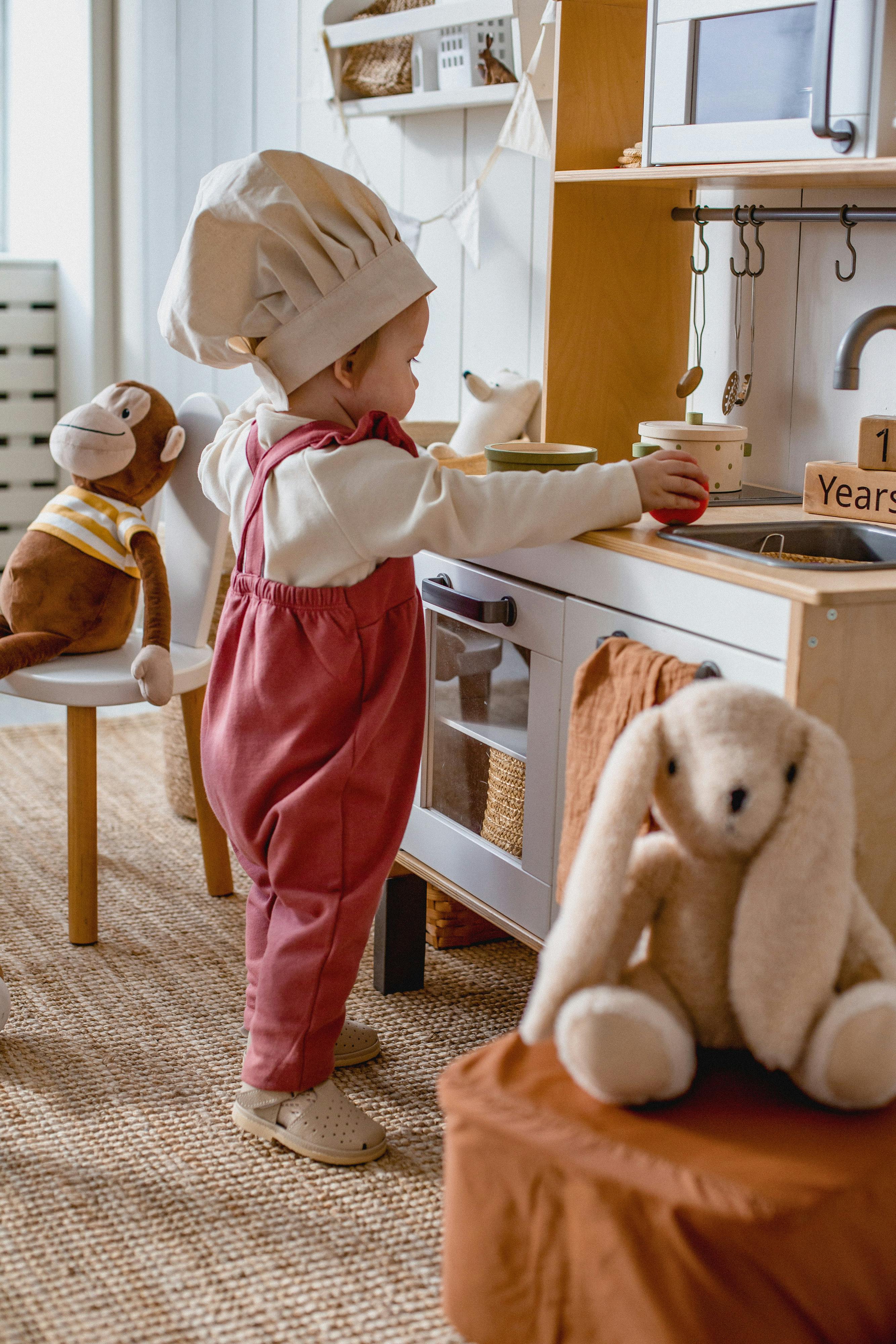 baby in a chef hat playing with a toy kitchen in a chef hat