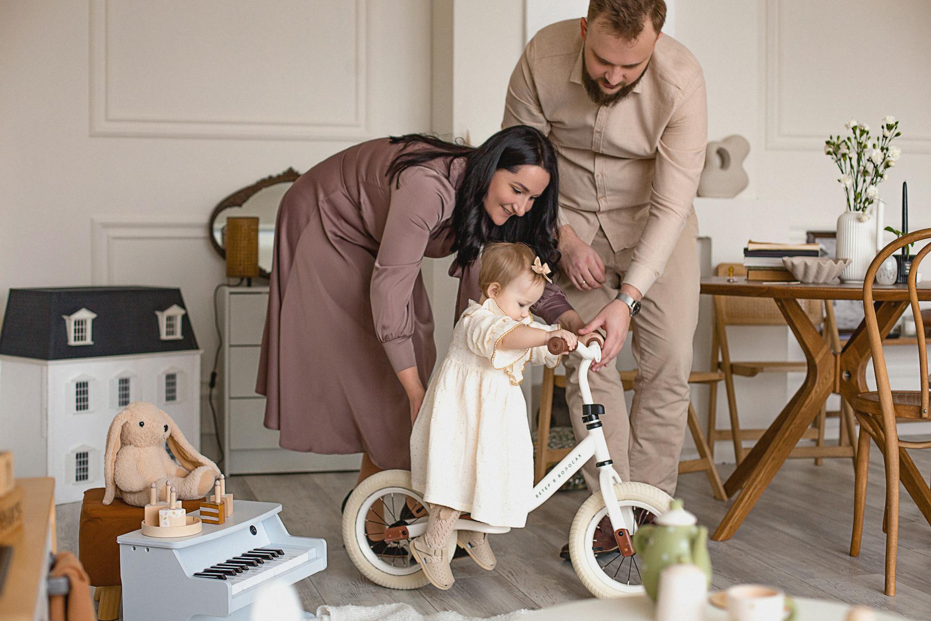 Happy parents helping their daughter ride a balance bike in a cozy living room setting, creating cherished family moments.