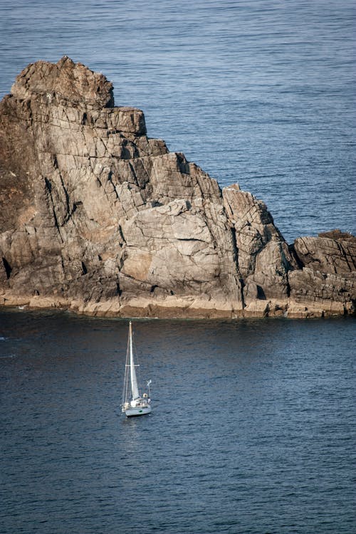 A sailboat is sailing in the ocean near a rock