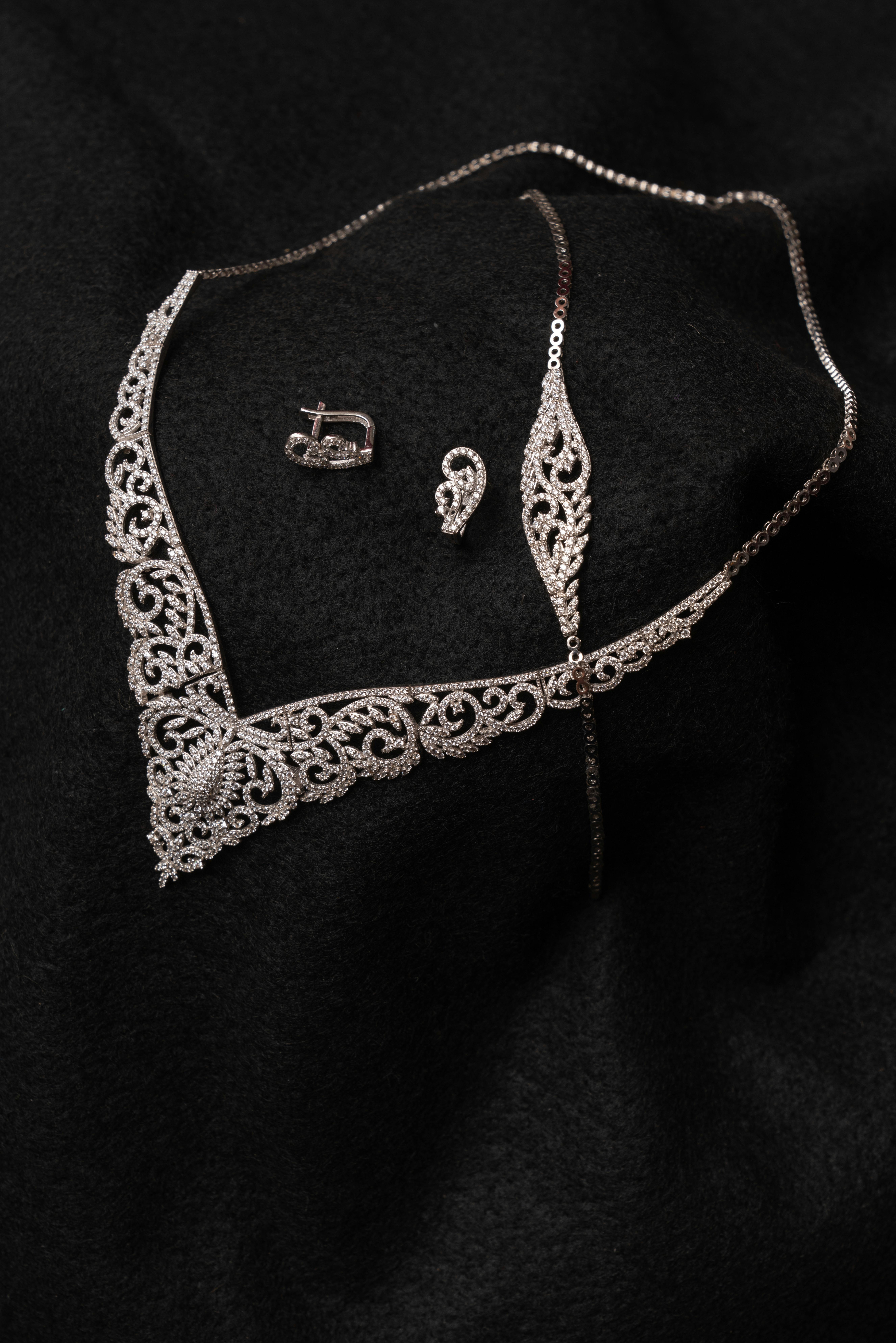Close-up of an intricate diamond necklace and earring set on black fabric background.