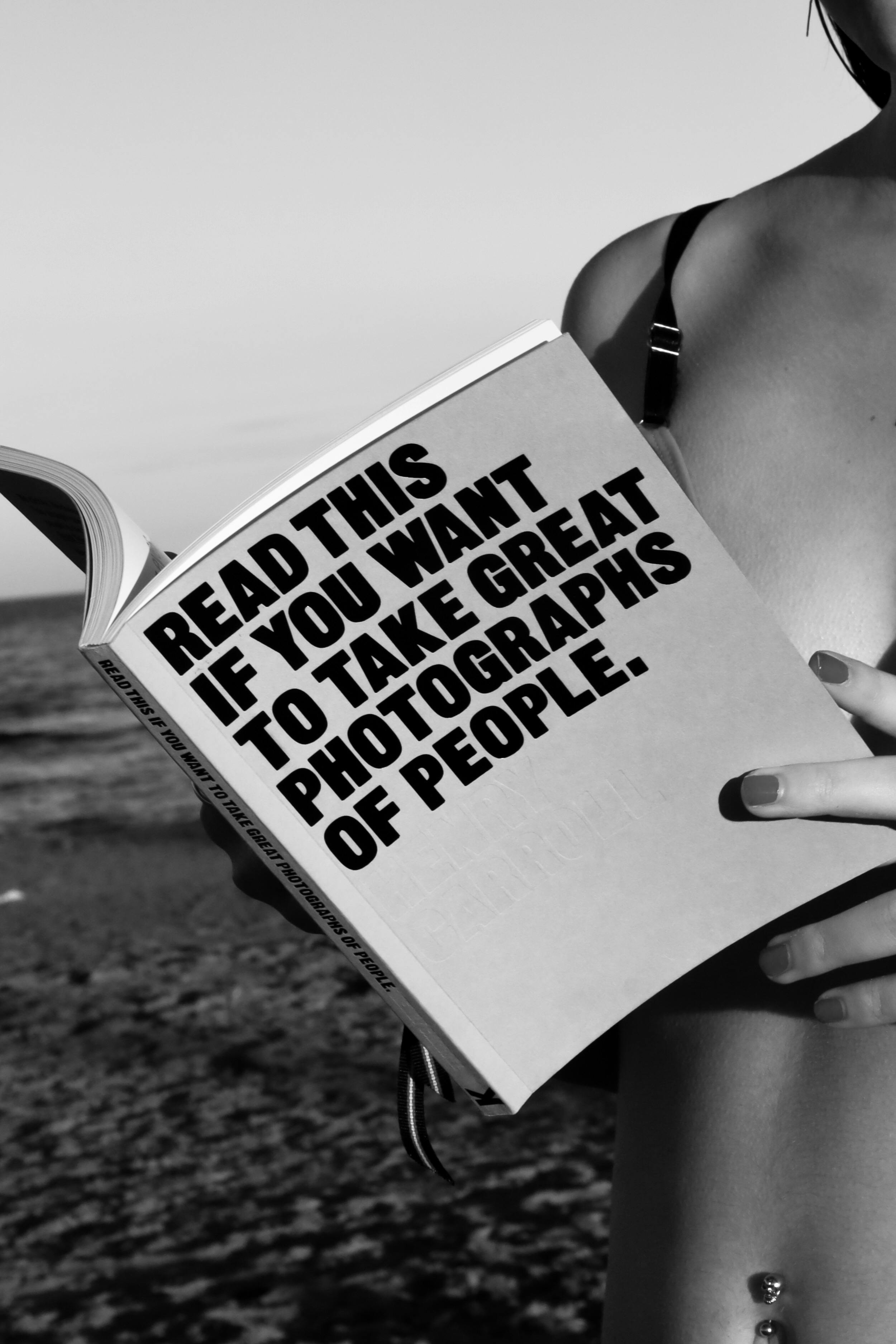 Black and white photo of a woman reading a photography book on a beach.