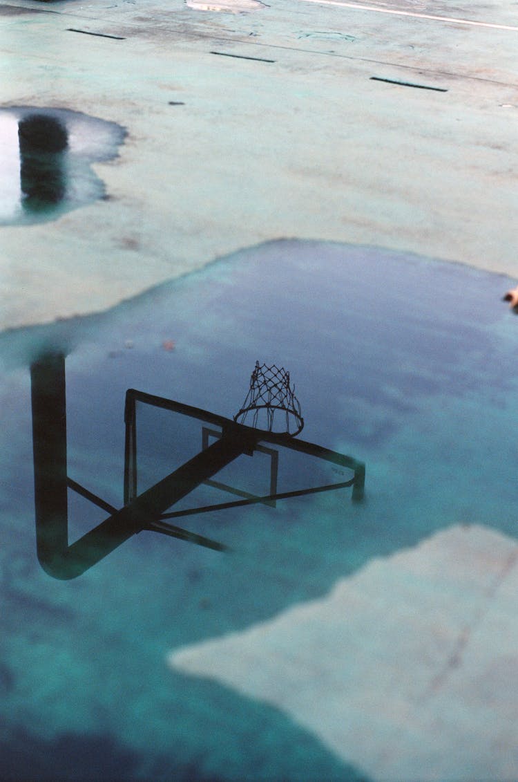 Reflection Of Basketball Ring With Net In Rain Puddle