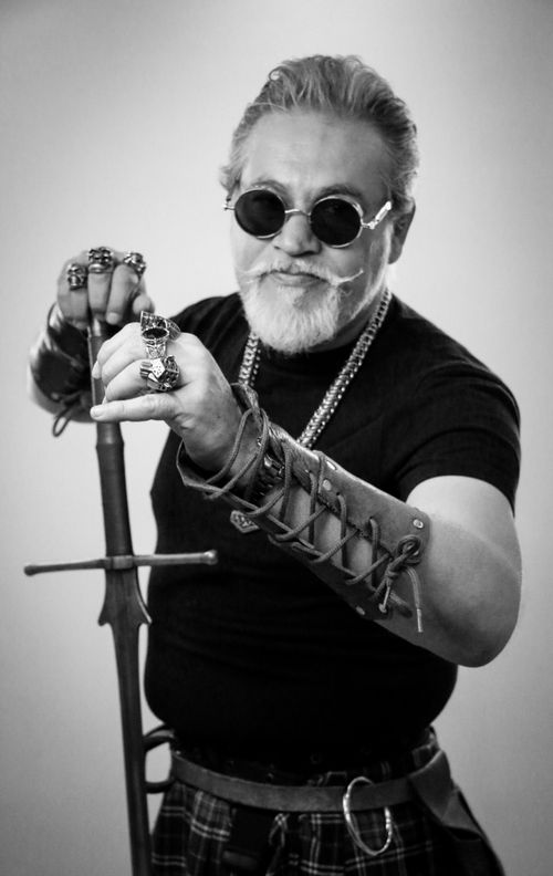 Free Portrait of a stylish man wearing sunglasses and jewelry holding a sword, conveying a bold and confident vibe. Stock Photo