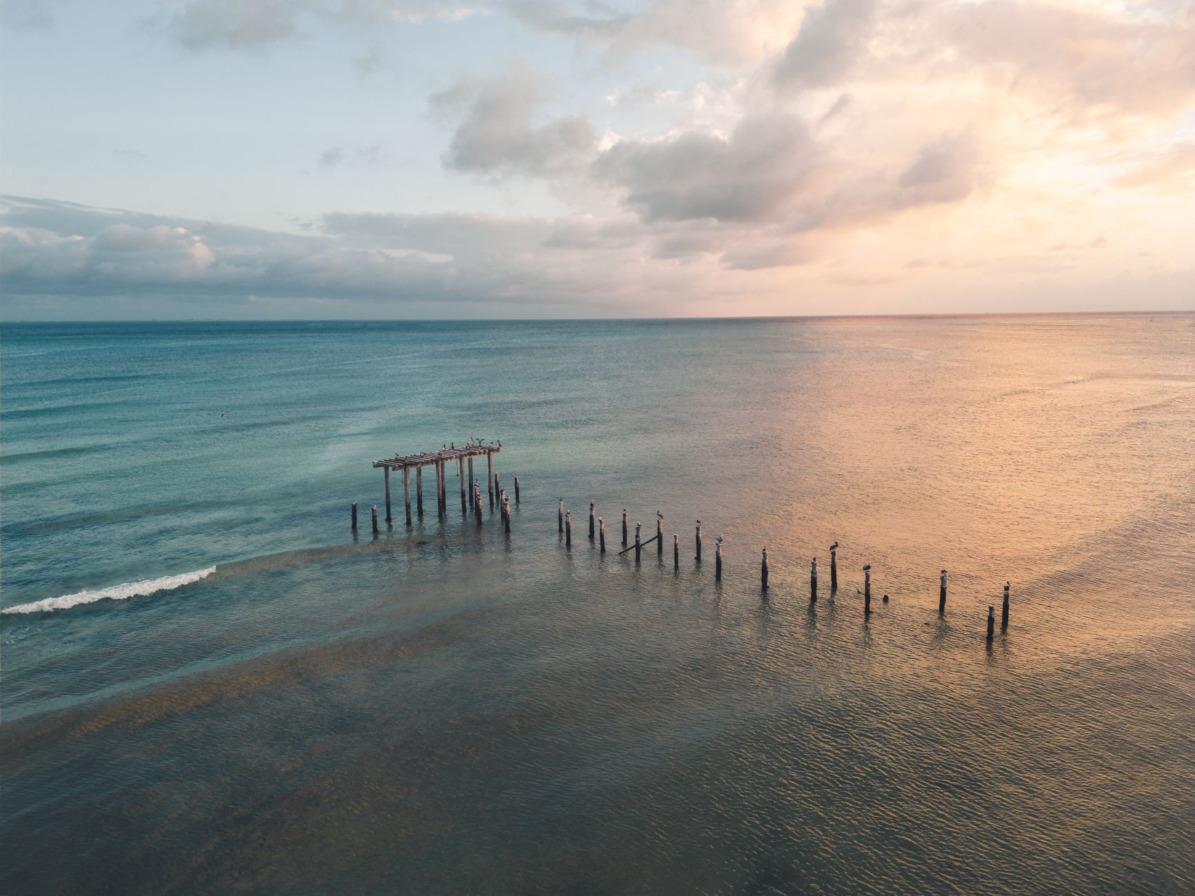 Dramatic sunset over the calm waters of Playa del Carmen with an aged pier in the foreground.