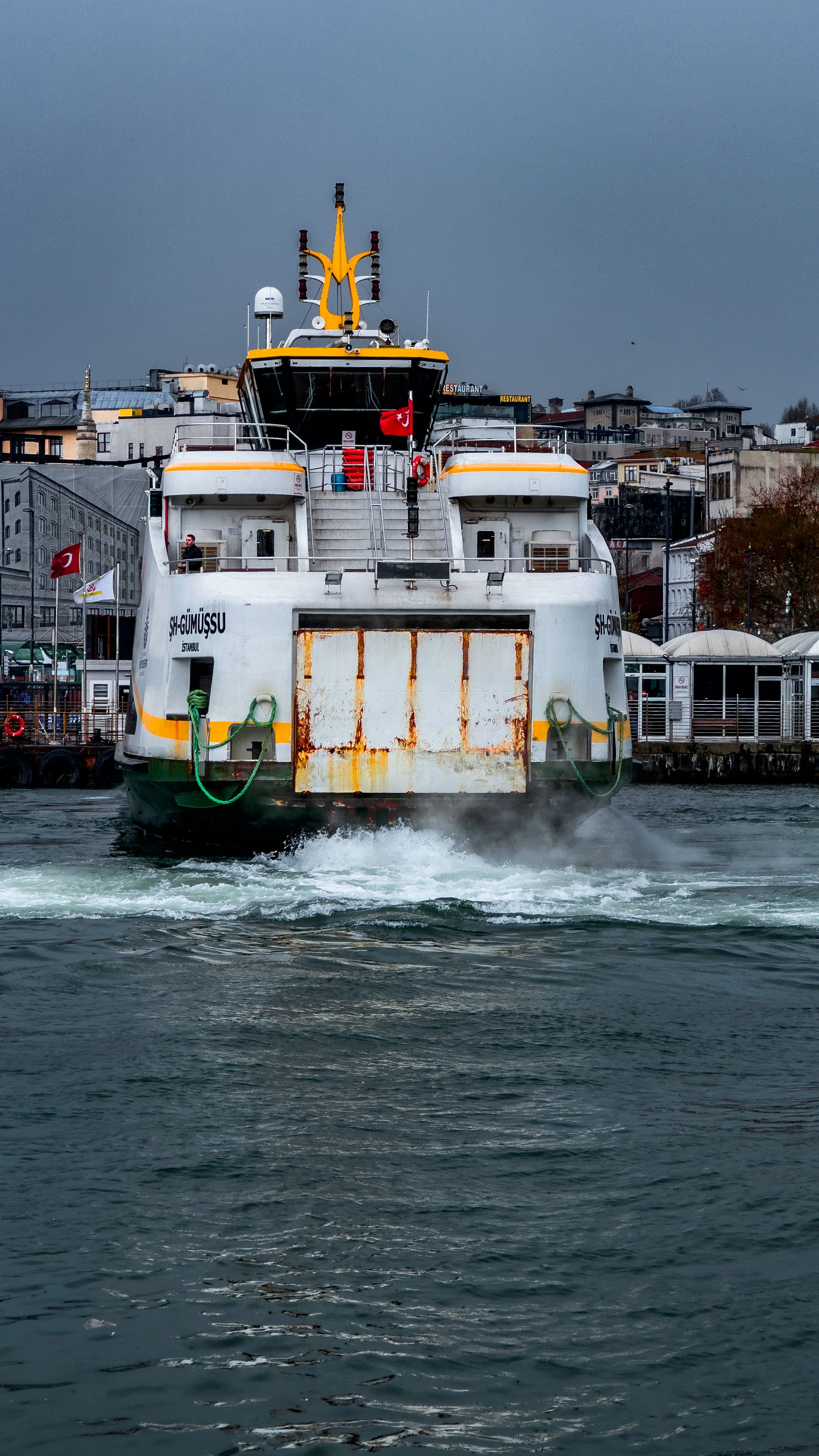 A ferry sails through the Istanbul harbor on an overcast day, Turkey's vibrant cityscape in the backdrop.