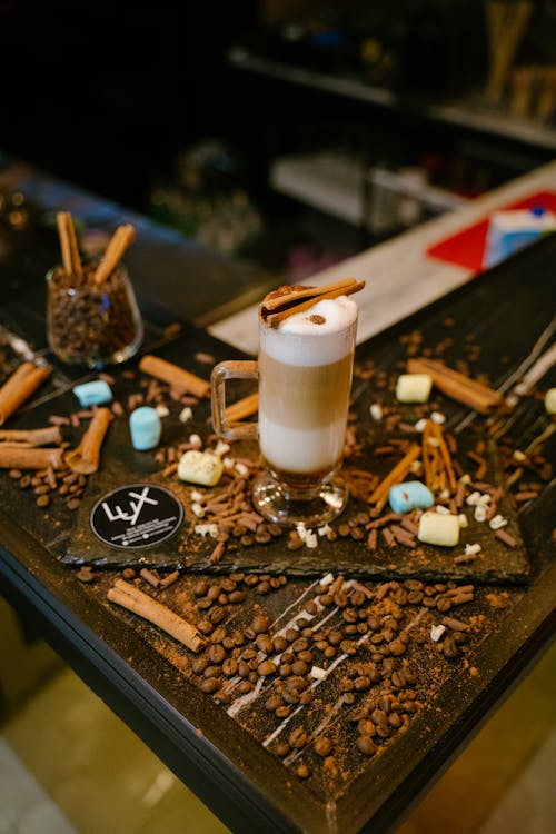 A Glass with Latte Macchiato Standing on a Table with Scattered Coffee Beans and Cinnamon Sticks