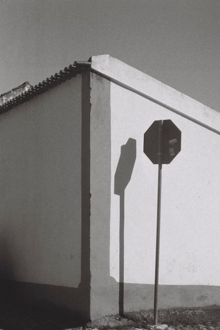 Minimalist black and white image of an urban scene in 脫bidos featuring a road sign and shadows on a building corner.
