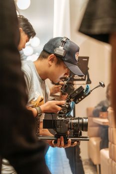 A cameraman in a cap intensely adjusts his filming equipment indoors, showcasing media production skills.