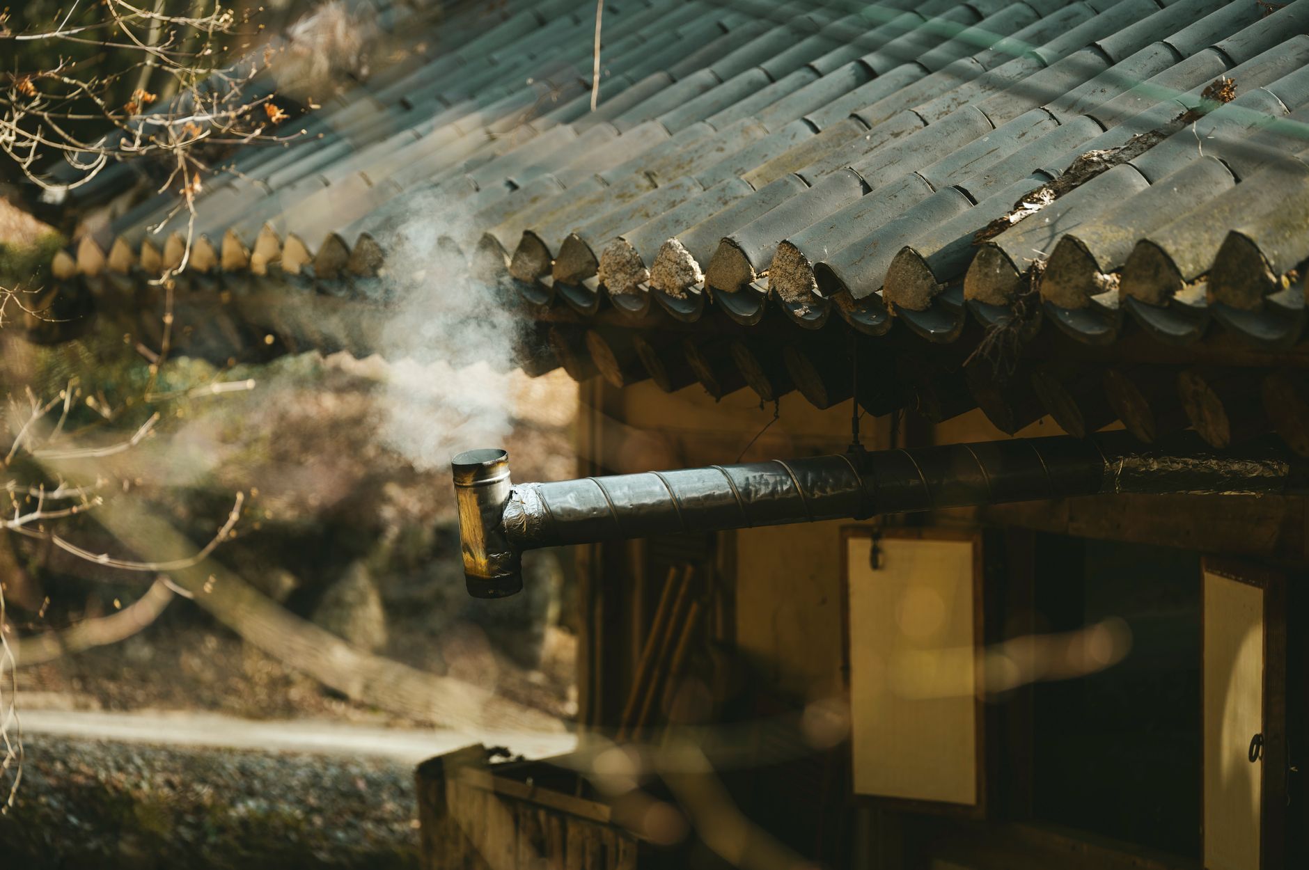 A rustic chimney releasing smoke on a traditional rural house roof, captured during daylight.