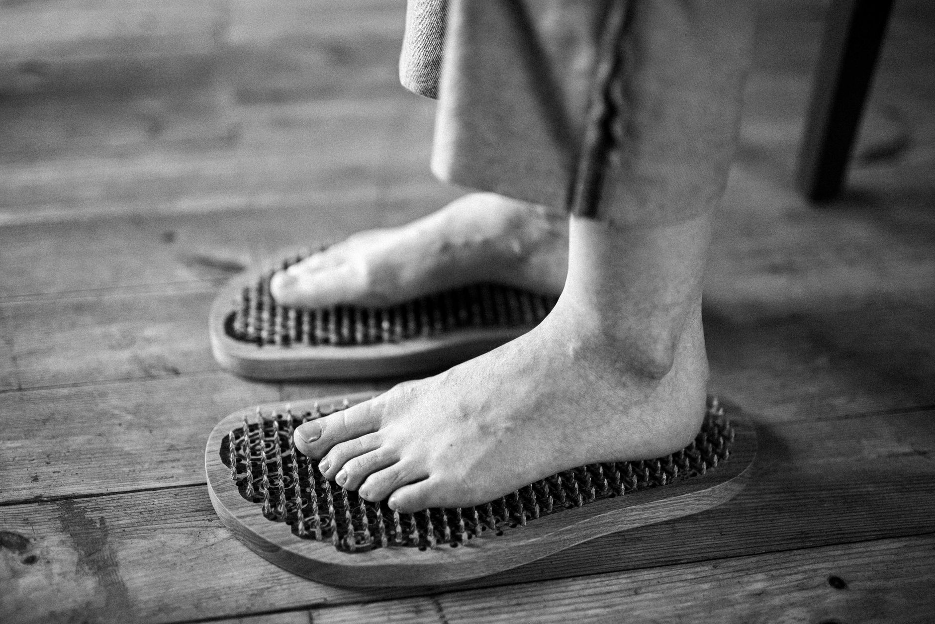 Black and white photo of feet receiving a relaxing massage on wooden reflexology boards.