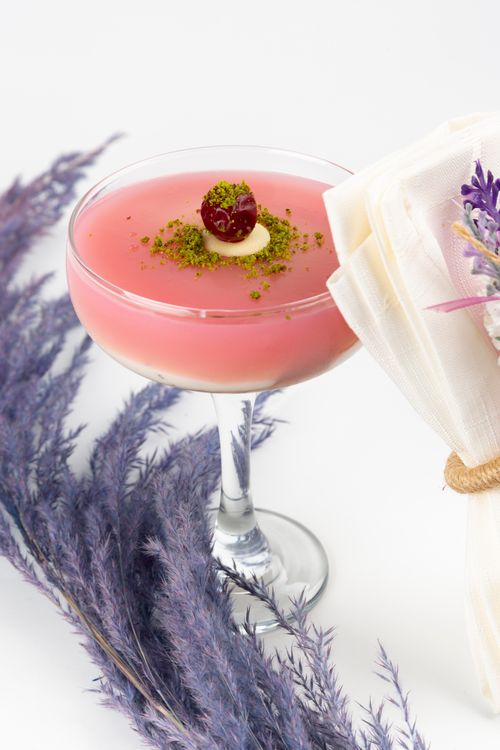 Free A delicate pink cocktail garnished with cherry and sprinkles, surrounded by lavender and napkin. Stock Photo
