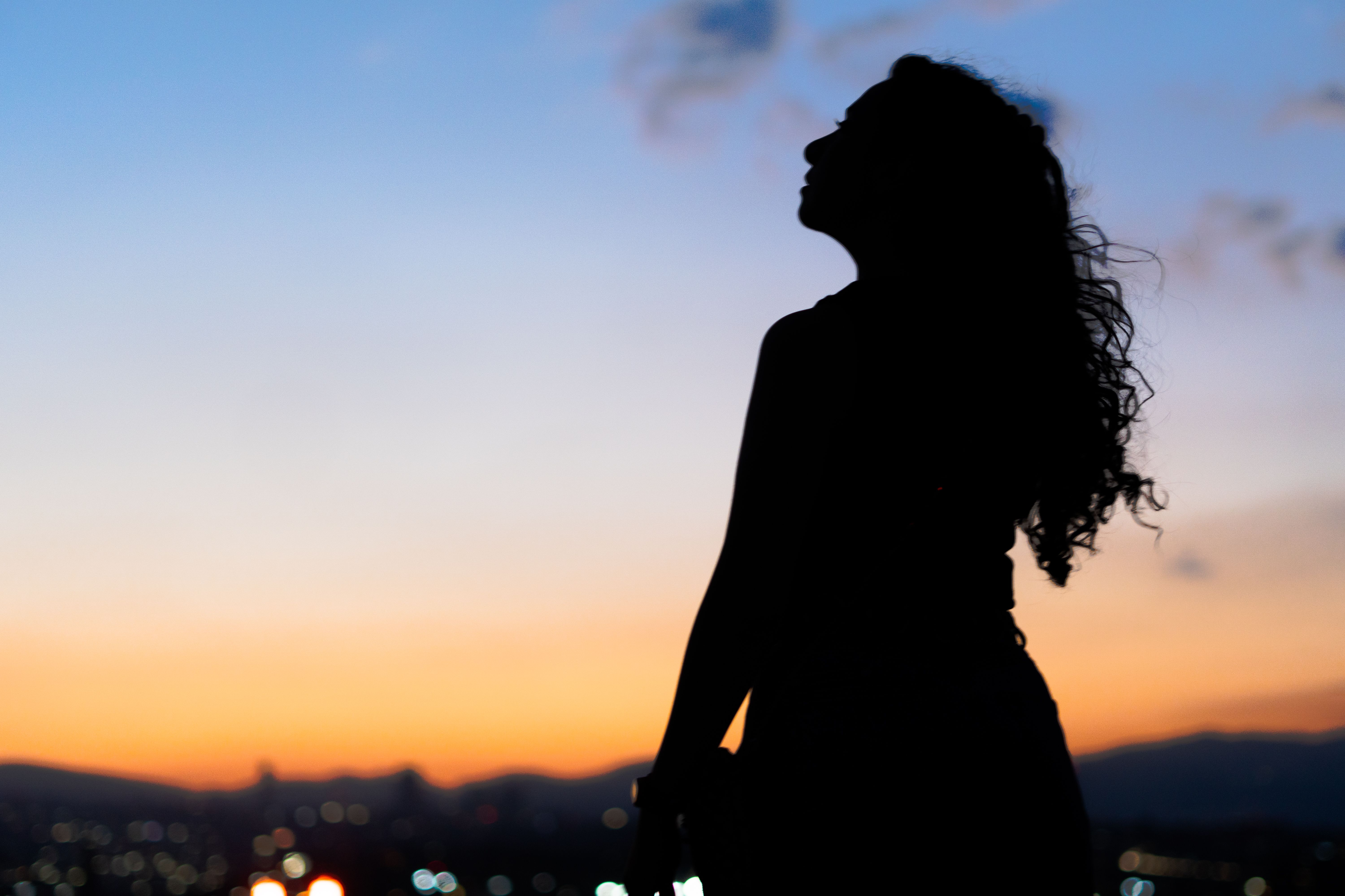 Silhouette of a woman with curly hair gazing at a vibrant Mexico City sunset.