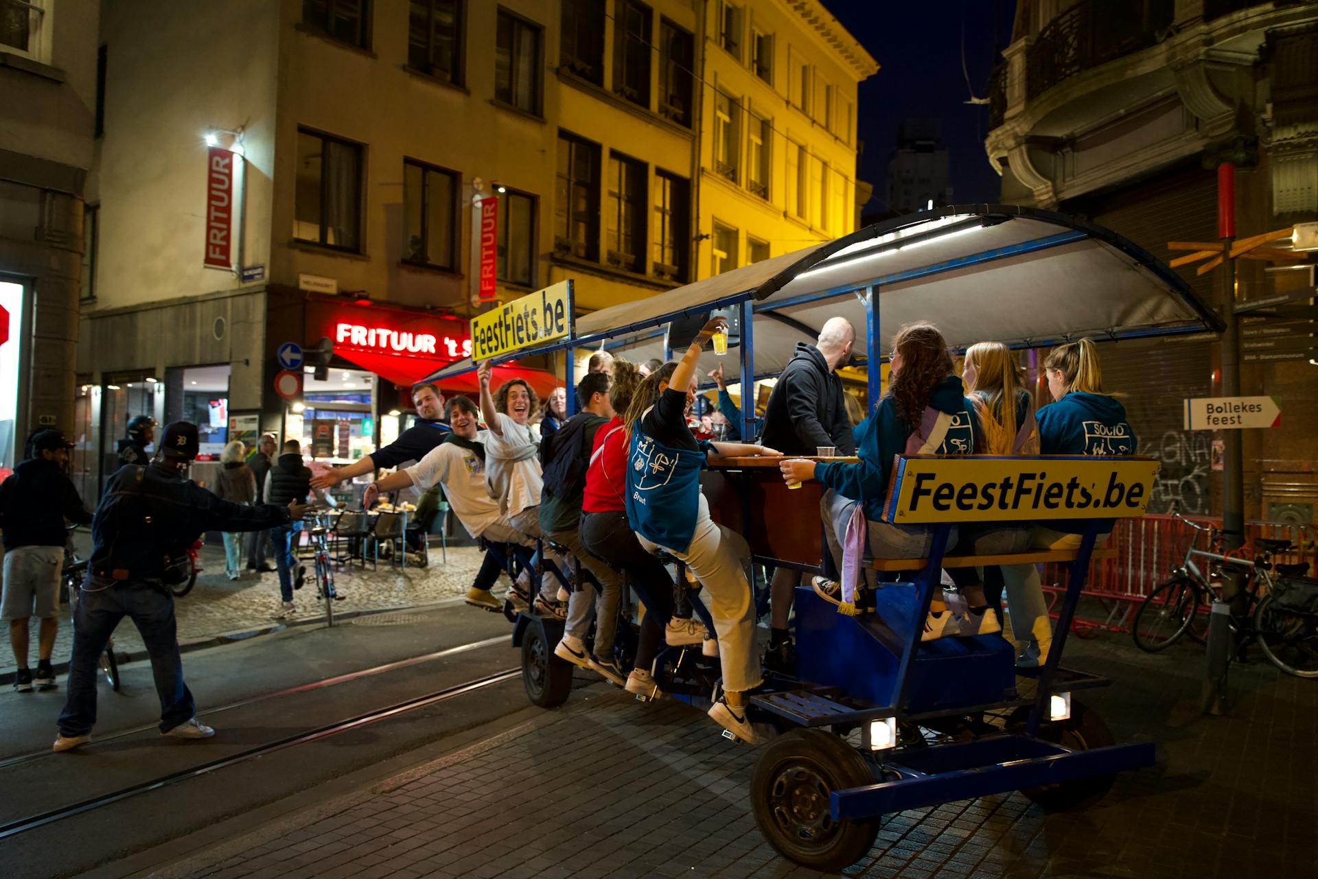 Group enjoying a night ride on FeestFiets in vibrant Antwerp street scene.