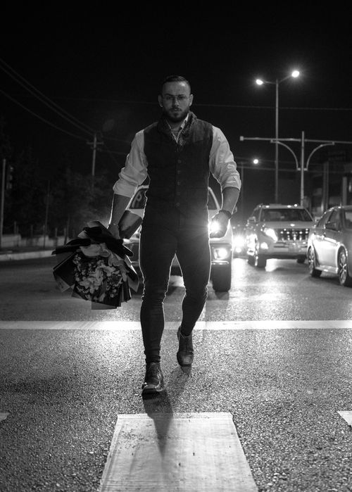 Free A man walks down a city street at night holding a bouquet with cars in the background, Sulaymaniyah, Iraq. Stock Photo