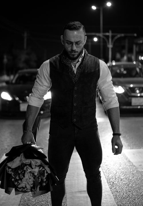 Free Black and white photo of a man in a vest carrying flowers on a city street at night. Stock Photo