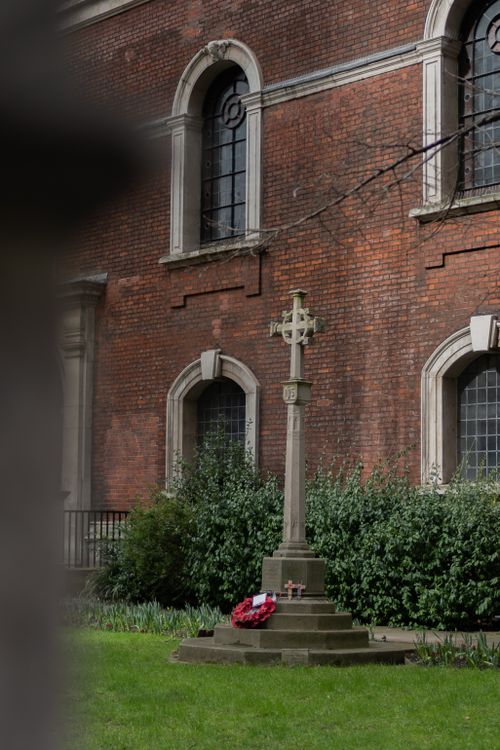 Free A classic stone cross in a historic church courtyard with red brick walls and windows. Stock Photo