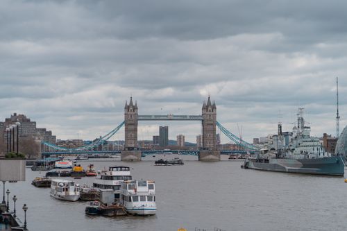 Free Atmospheric view of Tower Bridge over the Thames in London featuring boats and urban skyline. Stock Photo