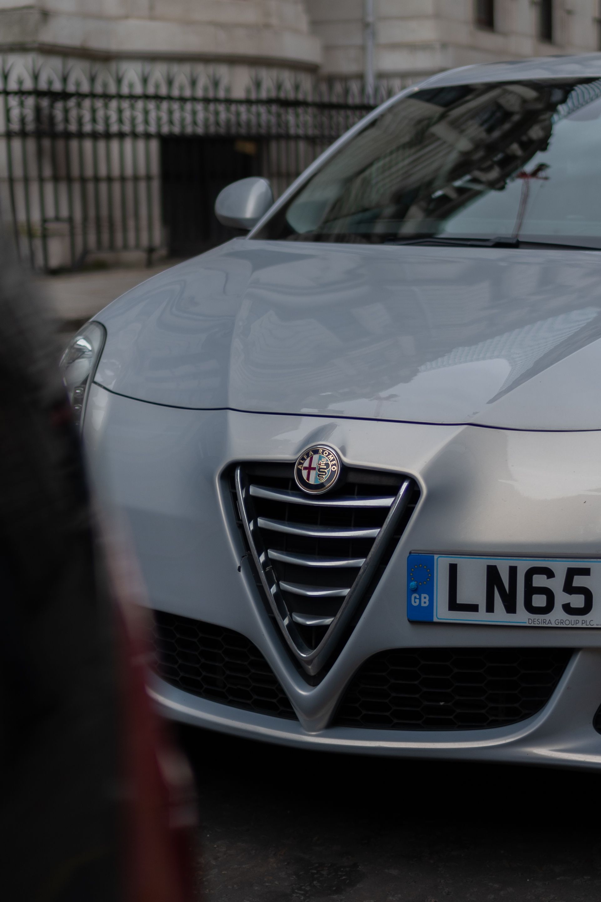 Detailed front view of a silver Alfa Romeo vehicle parked on an urban street.
