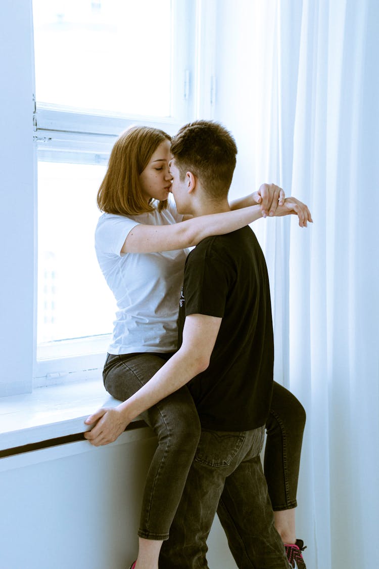 Woman Sitting On Windowsill Kissing Boyfriend