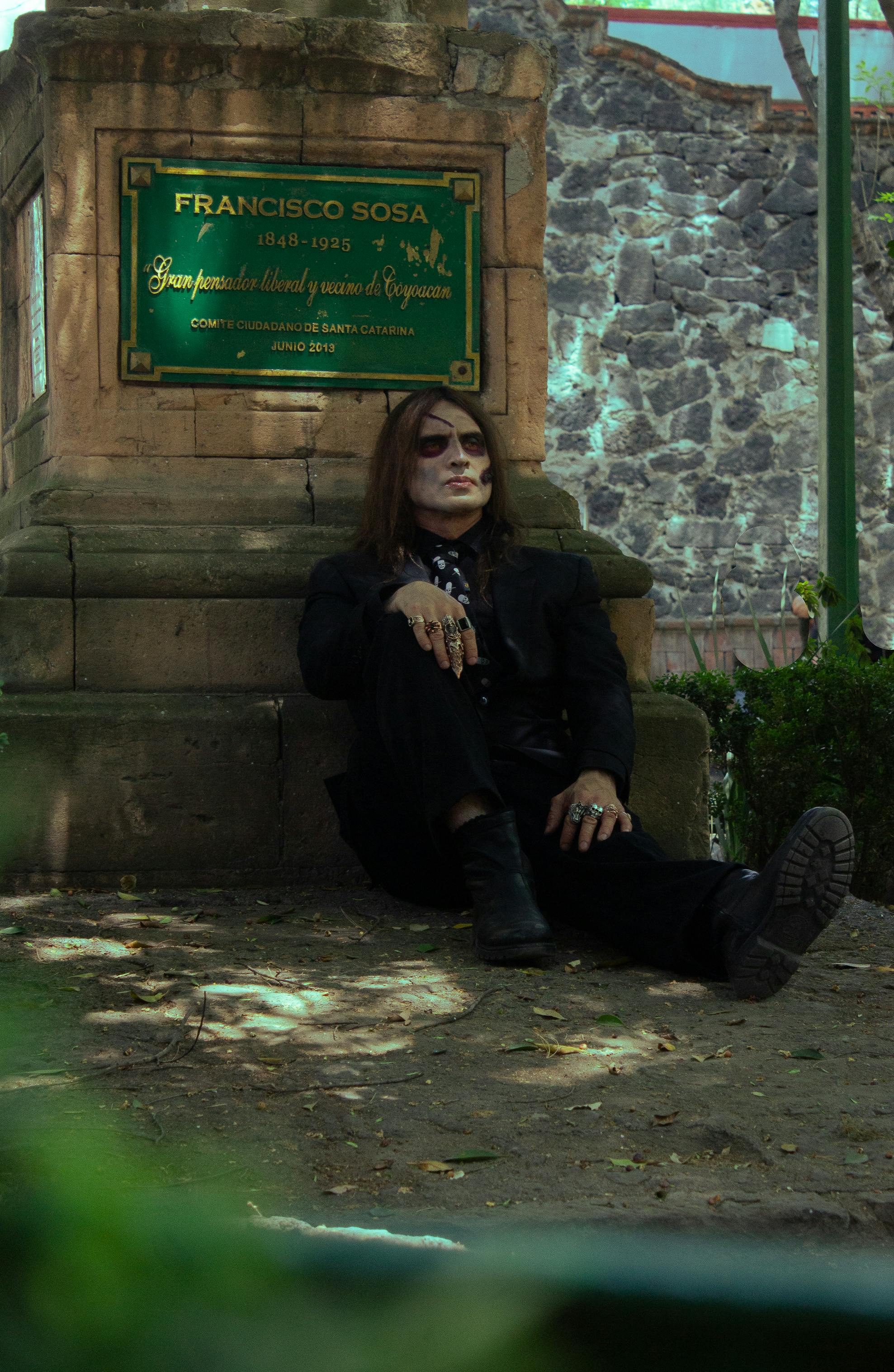 Person in Day of the Dead makeup resting by monument, capturing Mexican cultural essence.