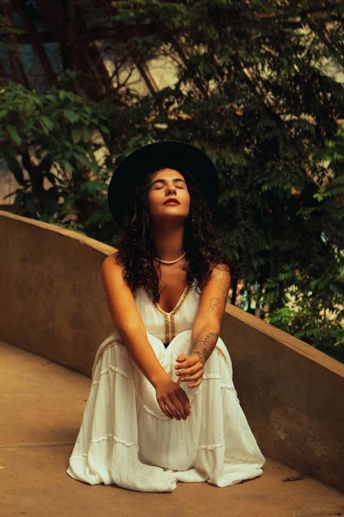 Pretty Brunette Wearing a White Dress Crouching Outdoors with Closed Eyes
