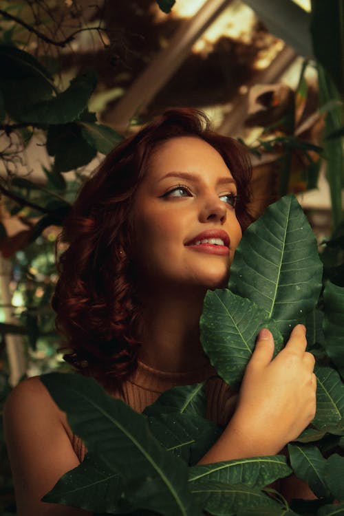 Portrait of a Pretty Redhead Standing Behind Green Leaves