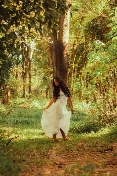 Free A young woman in a white dress walking gracefully through a lush sunlit forest. Stock Photo
