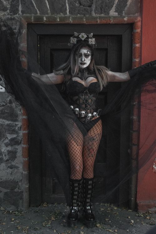 Free A woman in gothic costume with skull accents poses against a rustic door. Stock Photo