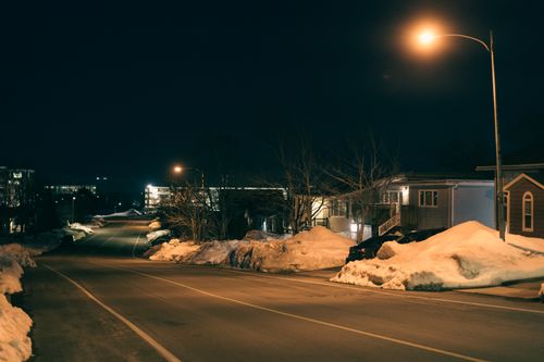 Free Snow-covered urban street at night illuminated by street lamps during winter, capturing a serene and calm atmosphere. Stock Photo