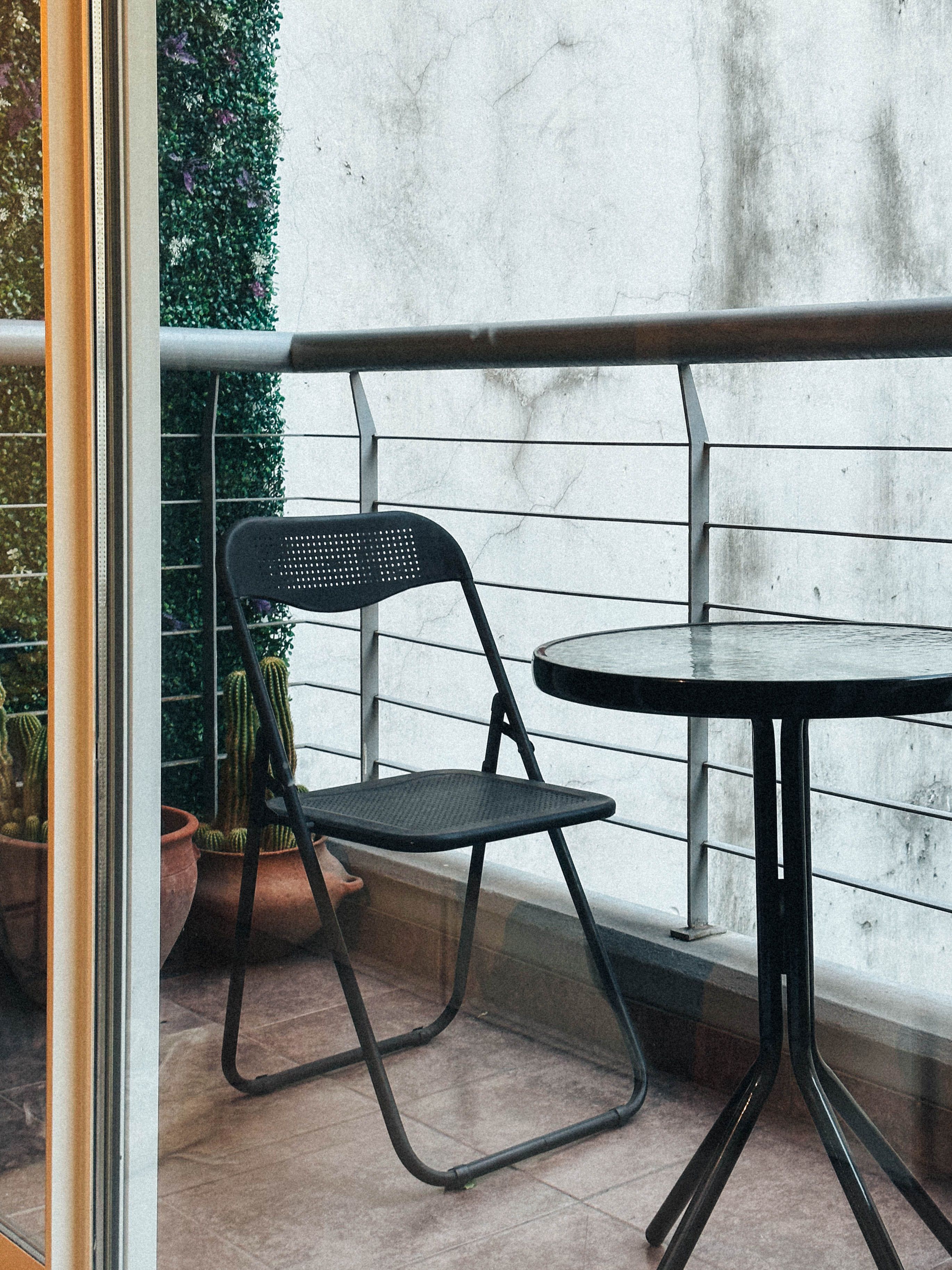Weather-resistant fold-down table mounted on a small apartment patio wall, folded open to hold a plant and coffee mug