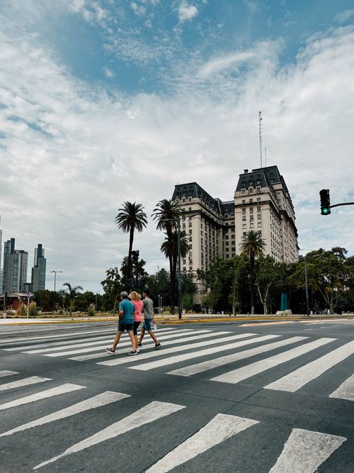 Free Urban scene in Buenos Aires with pedestrians crossing a zebra crossing near iconic architecture and palm trees. Stock Photo