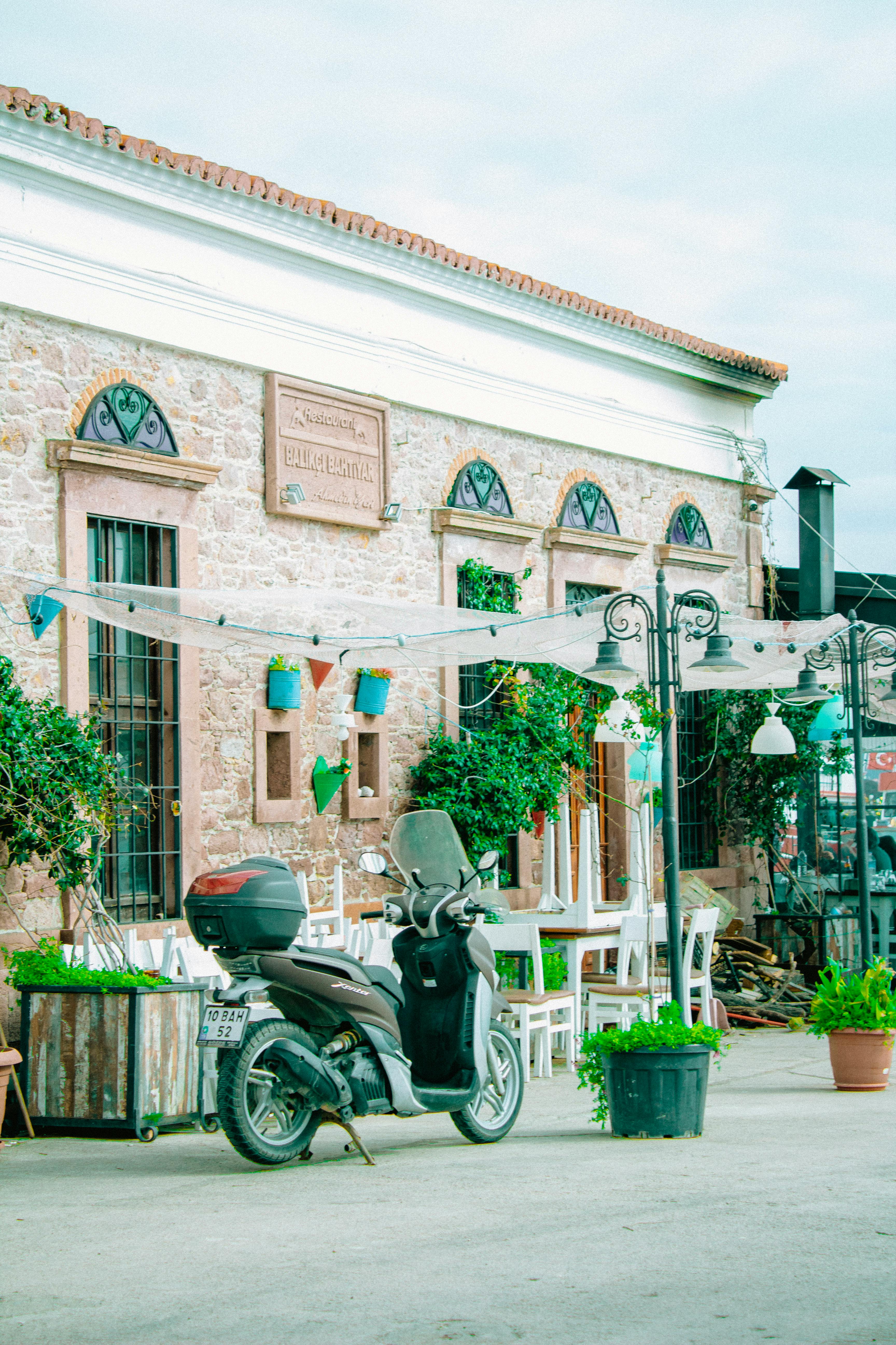 Free Outdoor urban scene with scooter, plants, and rustic building facade. Stock Photo