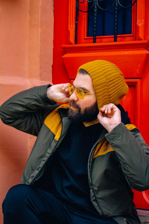Free Stylish bearded man with sunglasses and cap poses against a vibrant red backdrop. Stock Photo